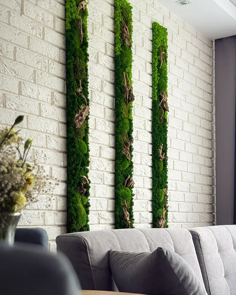 Trzy długie i wysokie obrazy bez ramy z zielonego mchu stabilizowanego na jasnej ścianie z cegły w nowoczesnym salonie w EverBloom Studio.